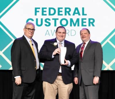 Three men are standing on stage in front of a screen reading "Federal Customer Award"