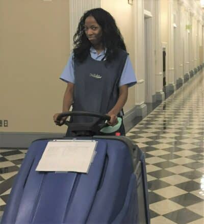 Anita is operating floor equipment. She is looking at the camera and smiling.