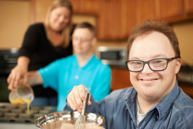 Man whisking with two adults cooking in background
