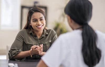 two women sitting at a table, facing each other and talking