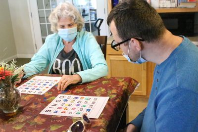 A woman on the left and man on right are sitting at a table, looking at their Bingo cards. 